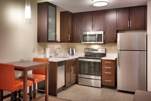 A modern kitchen with dark wooden cabinets, stainless steel appliances, and orange chairs.