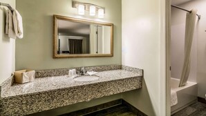Un baño con encimera de granito, lavamanos, espejo y cortina de ducha.