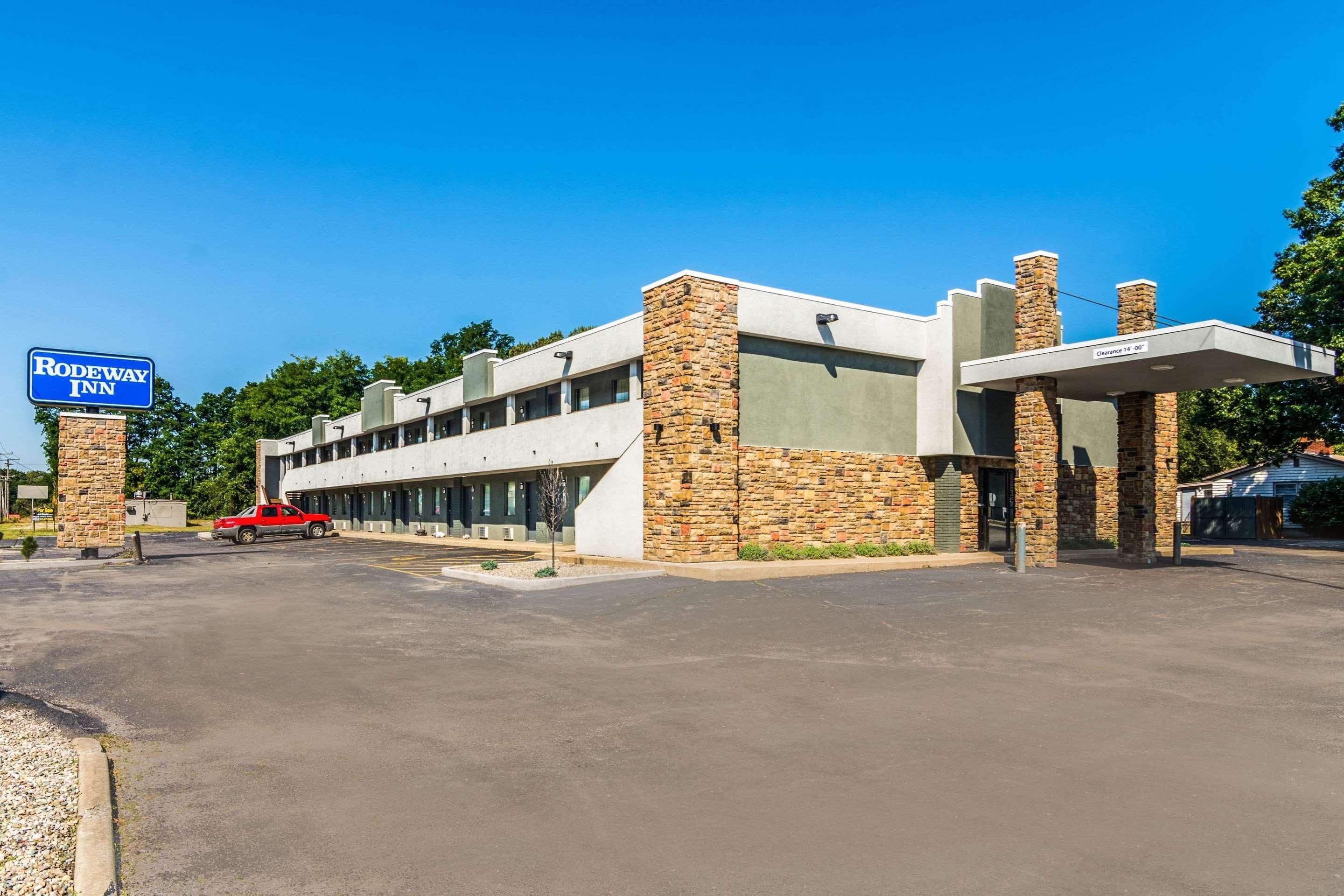 Un bâtiment moderne, sur lequel on peut voir une enseigne indiquant « Rodeway Inn », avec un parking et un véhicule rouge.