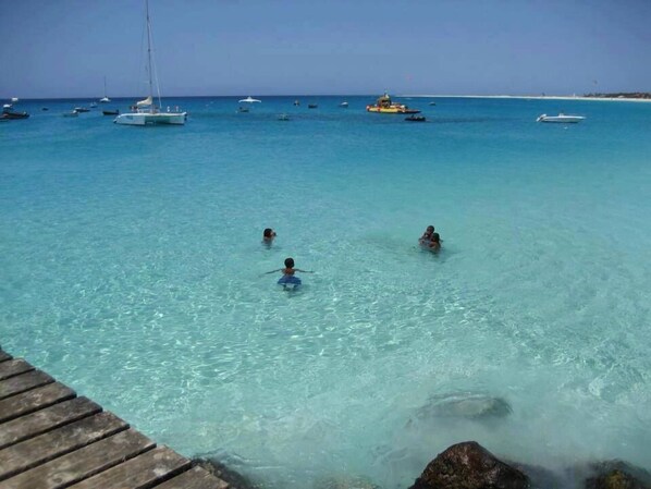 A clear turquoise sea with boats and a wooden dock.