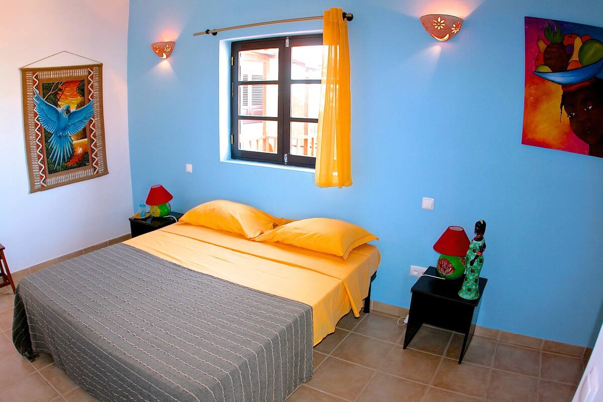 A bedroom with a bed, a window with curtains, a nightstand, and wall decorations.