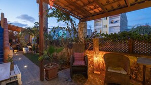 An outdoor patio with stone flooring, wooden furniture, and a pergola with vines. - Sakaroule Bed & Breakfast (Sal)