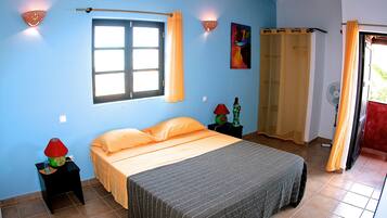 A bedroom with a bed, a window, a nightstand, a lamp, a fan, and a curtain.