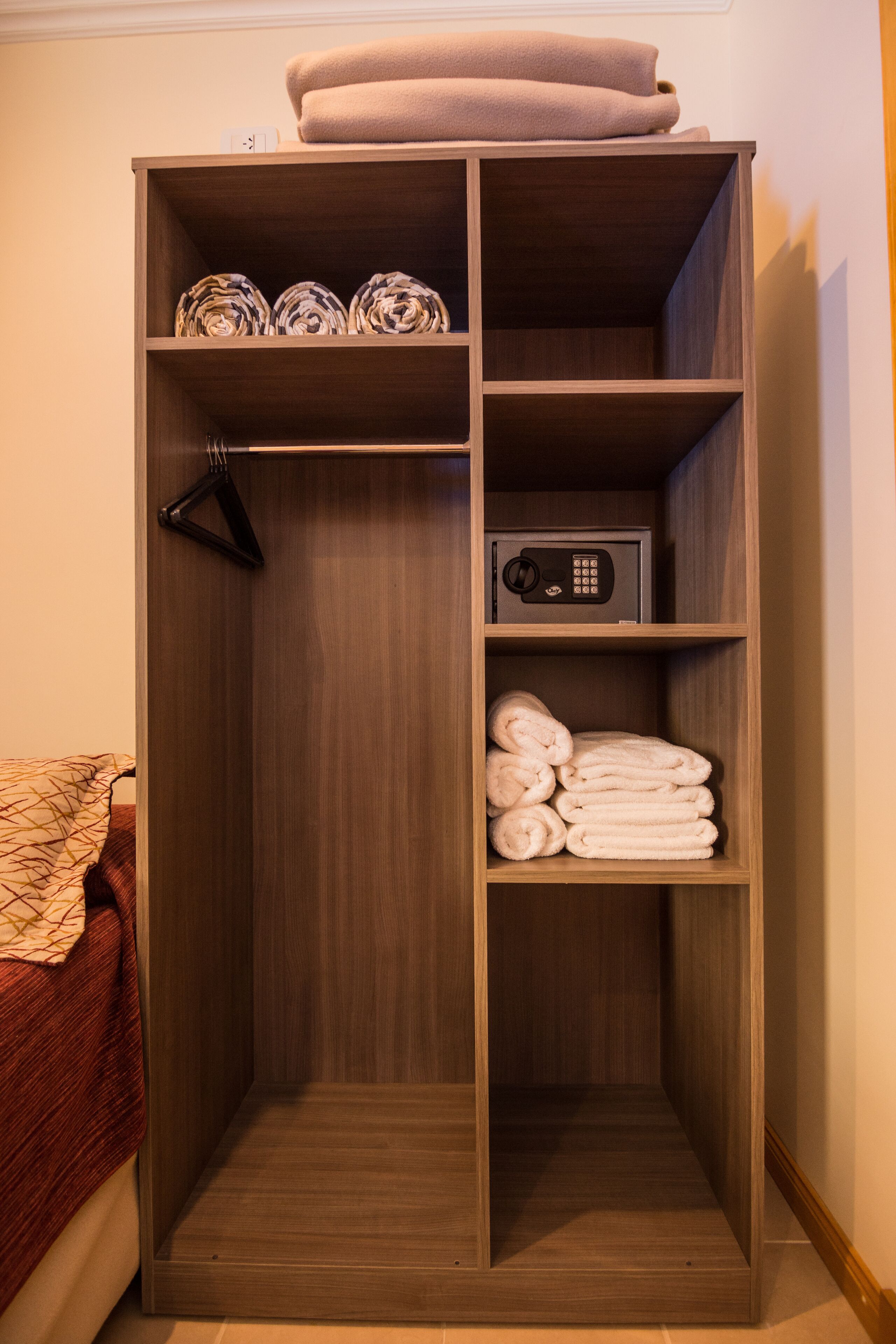 A wooden wardrobe with shelves, a hanging rack, and a safe.