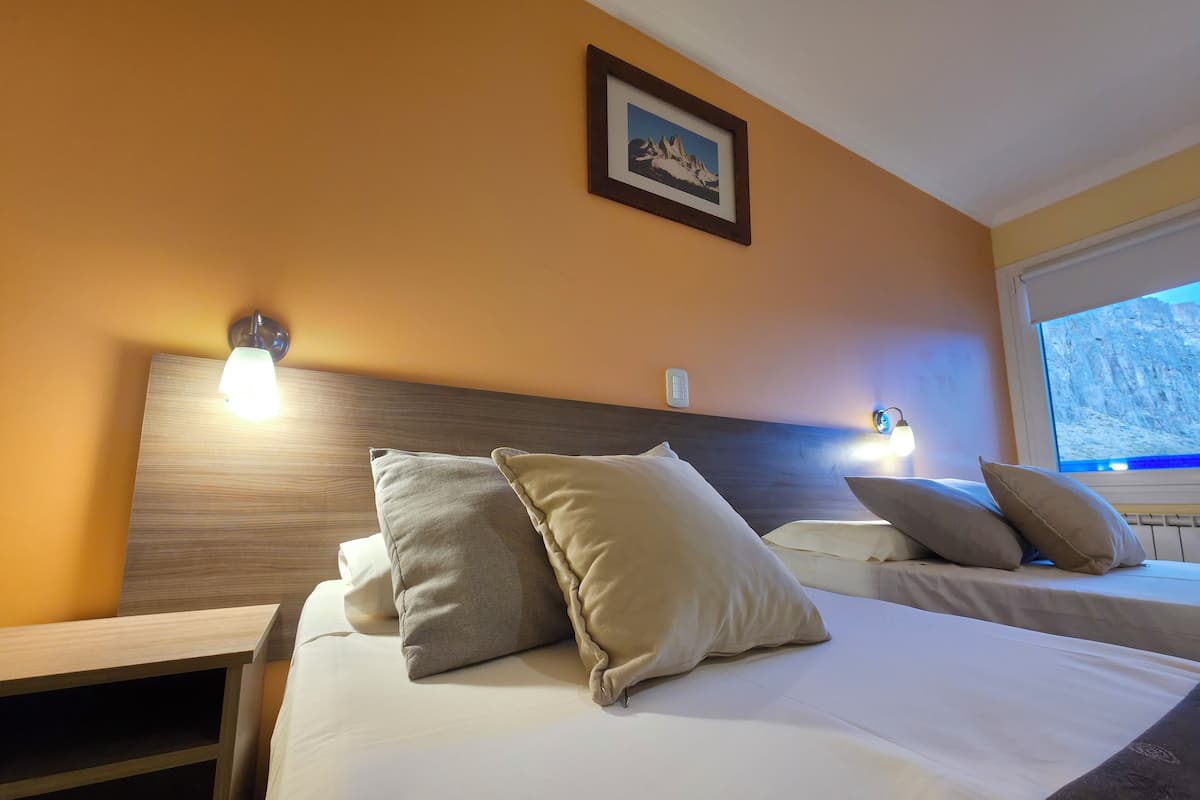 A hotel room with two beds, each with beige pillows, a wooden headboard, and a framed picture on the wall.