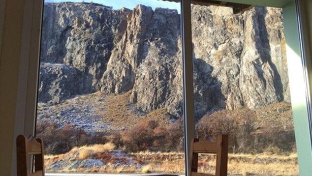 A room with a large window offering a view of rocky terrain and sparse vegetation. - Vertical Lodge (El Chalten)