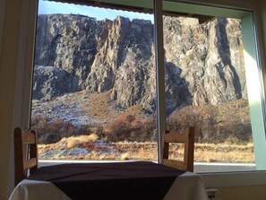 A room with a large window offering a view of rocky terrain and sparse vegetation. - Vertical Lodge (El Chalten)