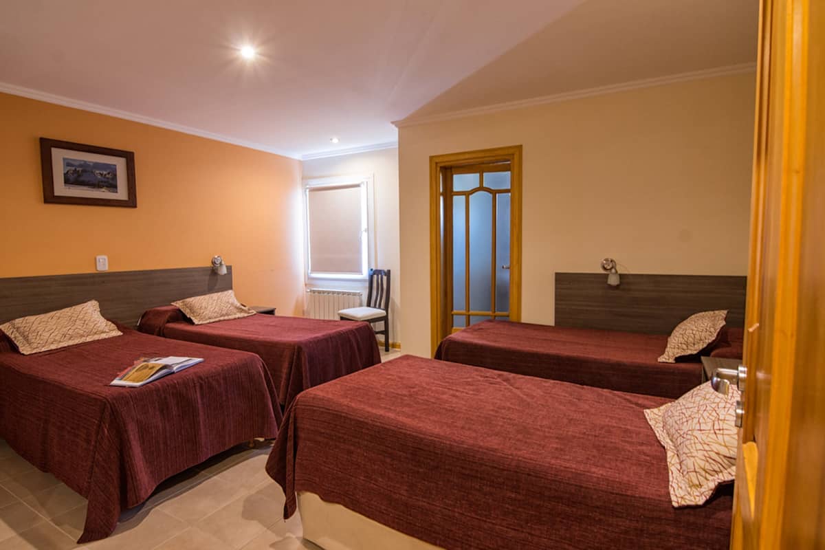 A hotel room with three single beds, a chair, a radiator, and a door with a glass panel.