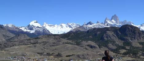 A woman standing on a rocky outcrop overlooking a town with snow-capped mountains in the background.