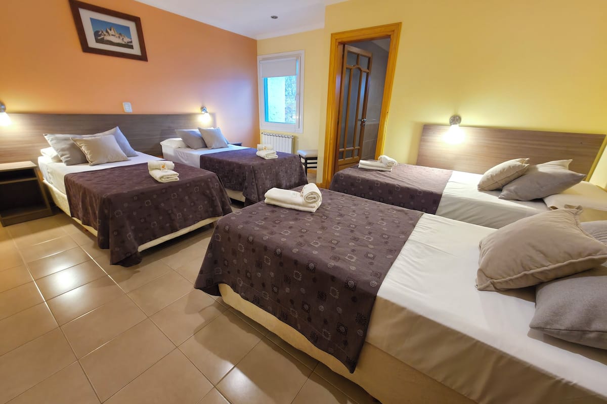 A hotel room with four beds, each with a headboard and pillows, and a window with a view.