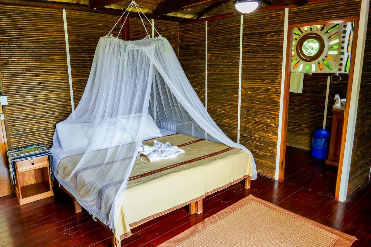 Een bed met klamboe, houten wanden, een klein nachtkastje en een wandklok.