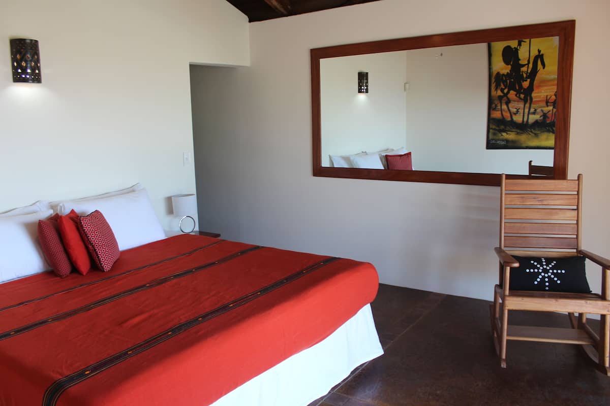 Een slaapkamer met een groot bed, een houten stoel, een schilderij aan de muur en een nachtkastje.