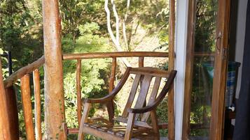 Una terraza de madera con una mecedora, un ventanal de vidrio y vistas al verdor.