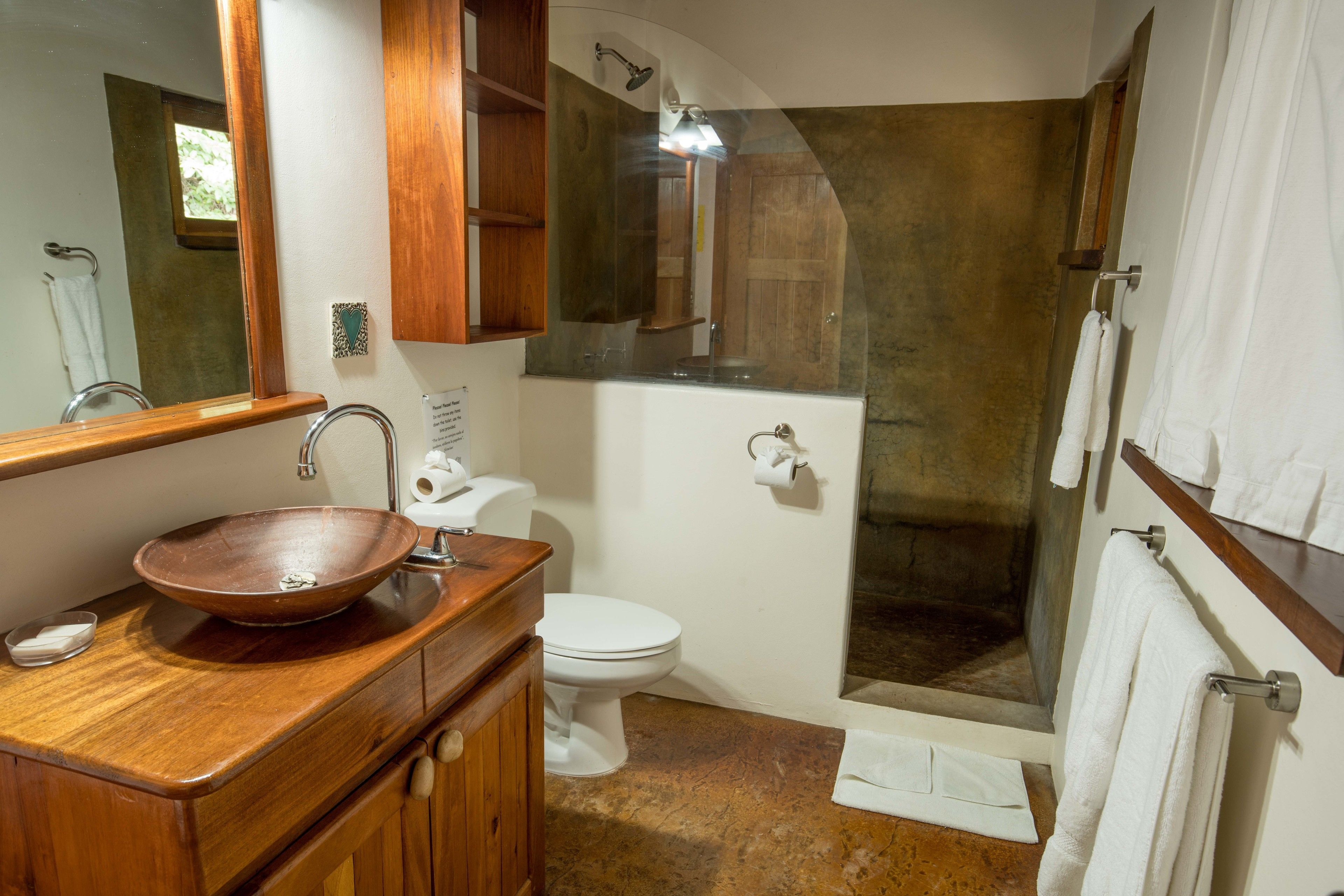 Un baño con tocador de madera, lavamanos blanco, inodoro y zona de ducha con mampara de cristal.