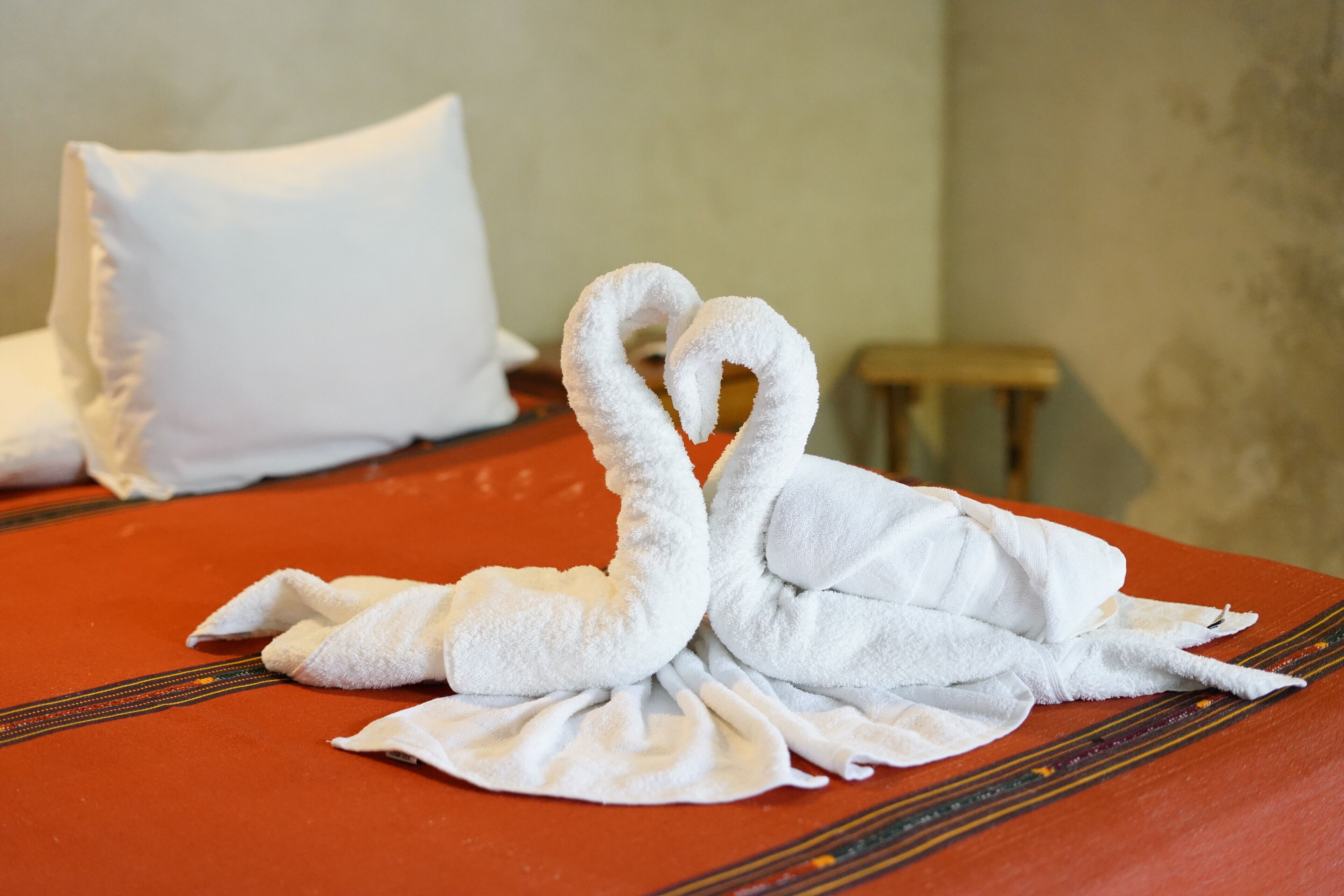 Una cama con un diseño de cisne hecho de una toalla blanca, una almohada blanca y un taburete de madera pequeño.