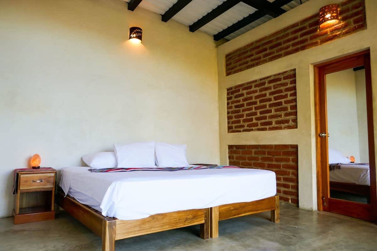 Een slaapkamer met een houten bed, een nachtkastje met een lamp en een bakstenen muur.