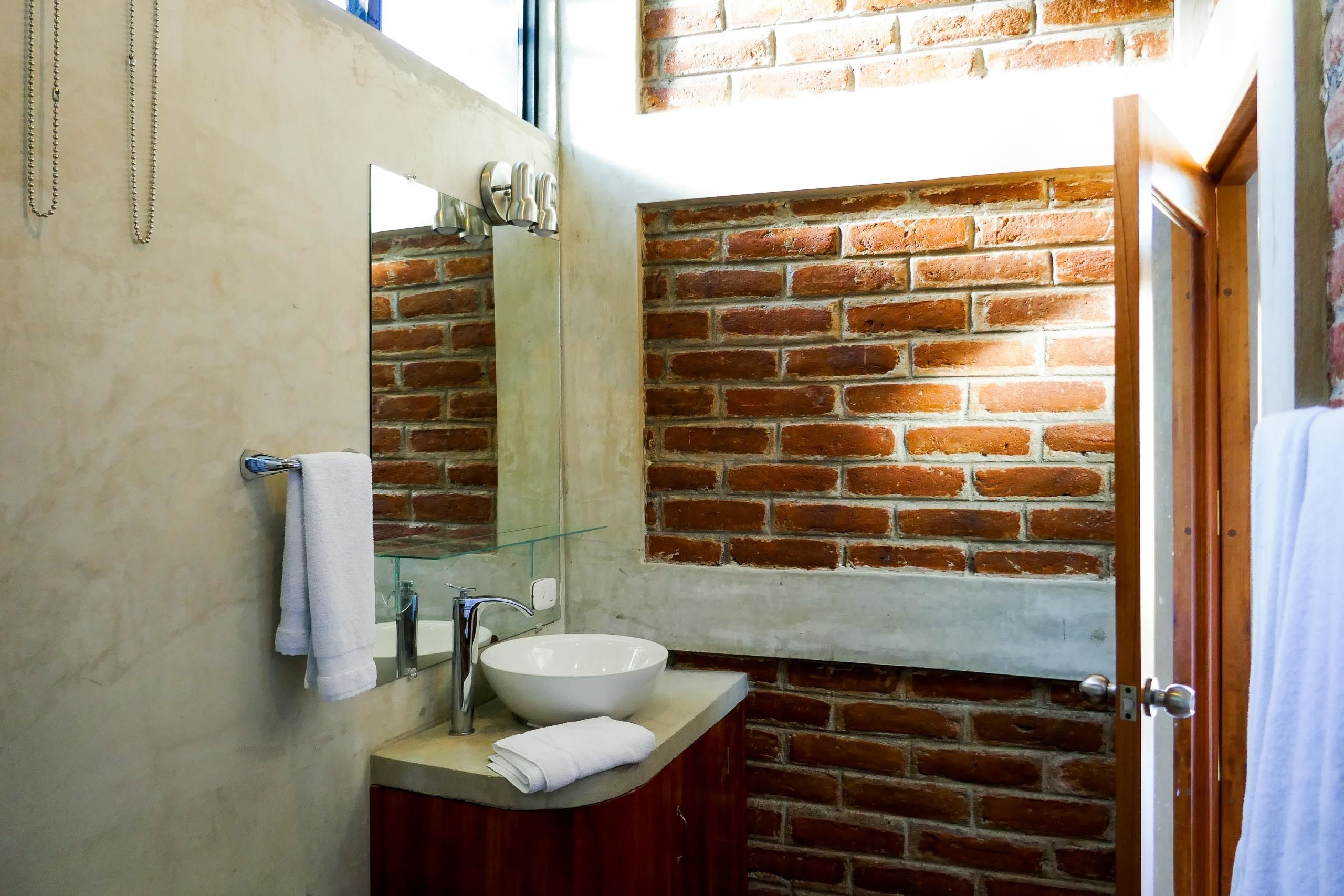 A bathroom with a white sink, a glass mirror, and a brick wall.