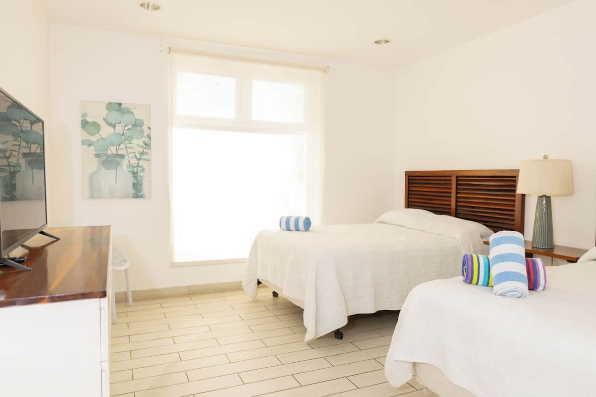 Camera d'albergo con due letti, una scrivania, una sedia, una finestra e un quadro appeso al muro.