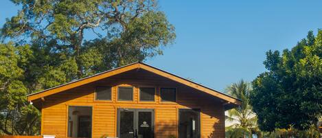 A wooden lodge with a front entrance, a porch, and a large tree in the background.