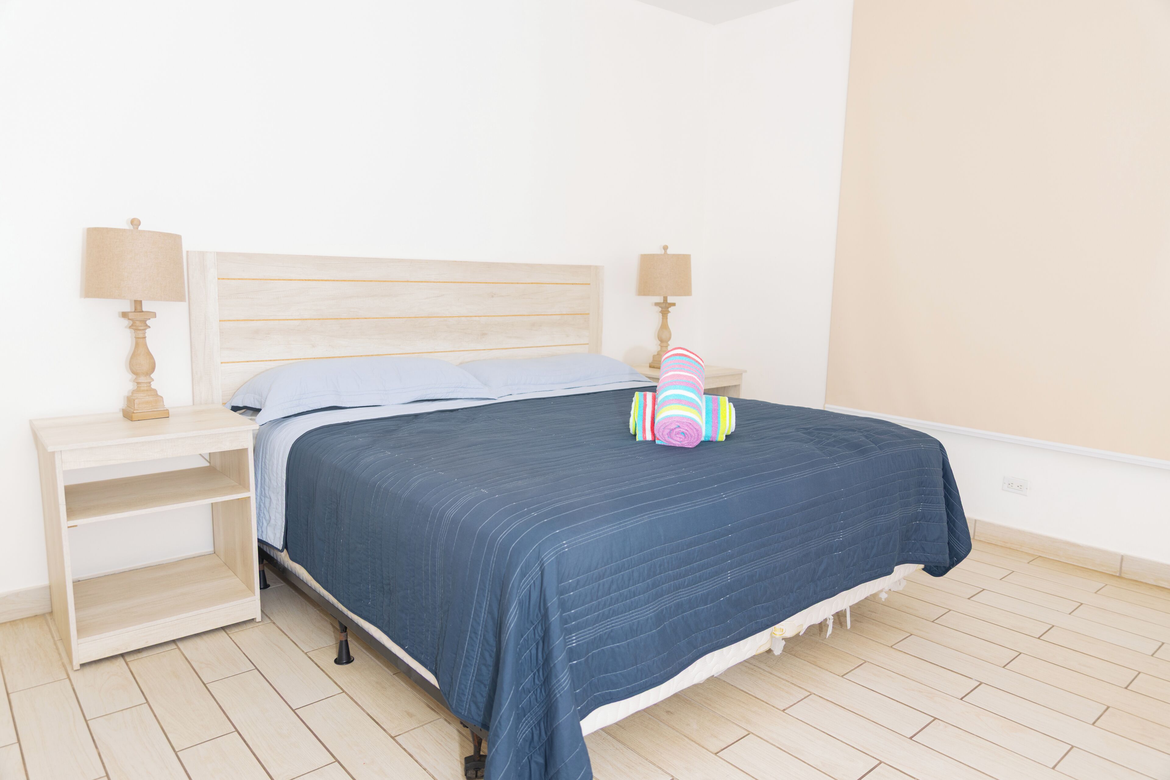 A bedroom with a bed, two bedside tables with lamps, a wooden nightstand, and a wooden floor.