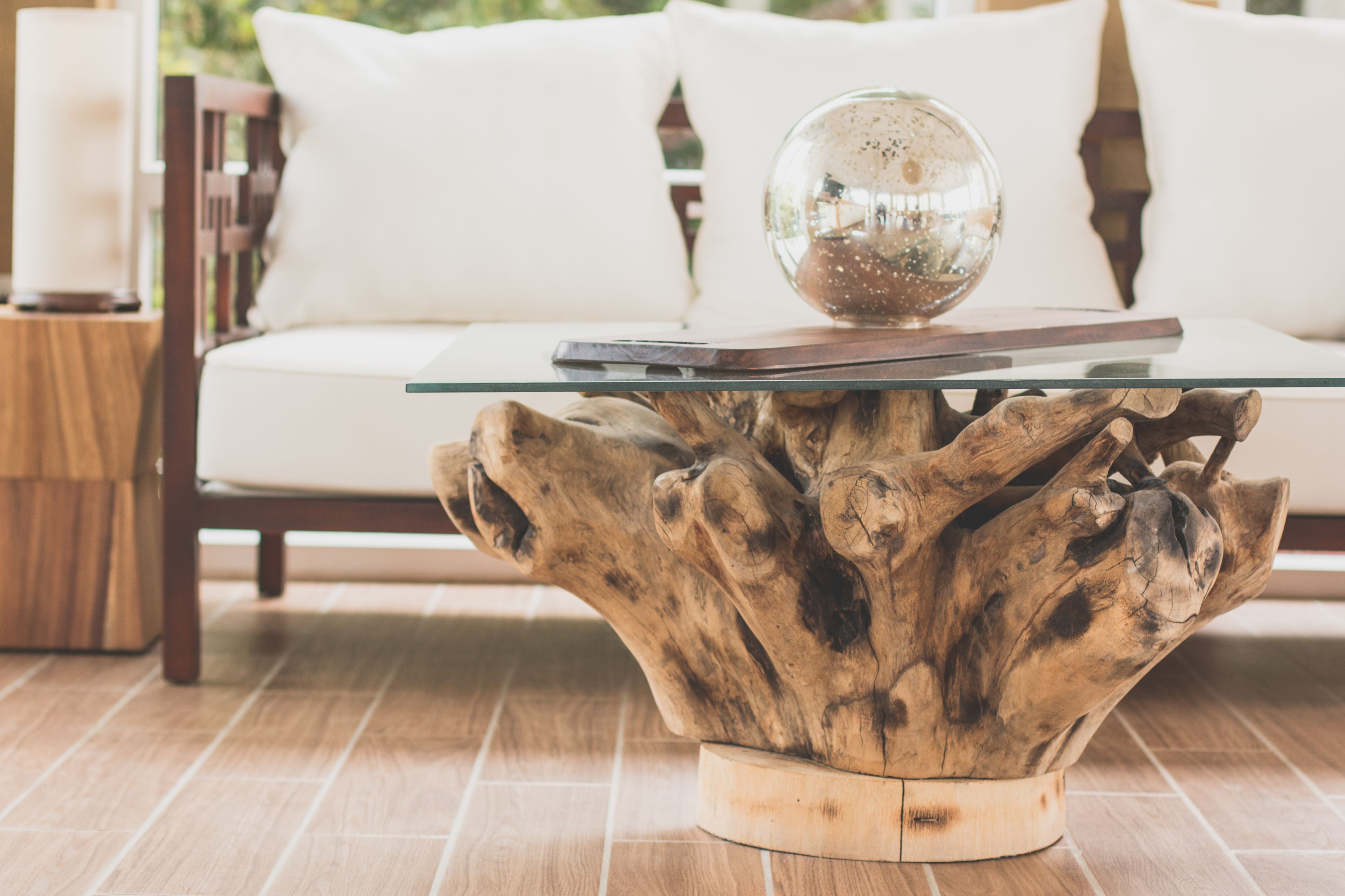 A wooden coffee table with a glass top, placed on a tiled floor.