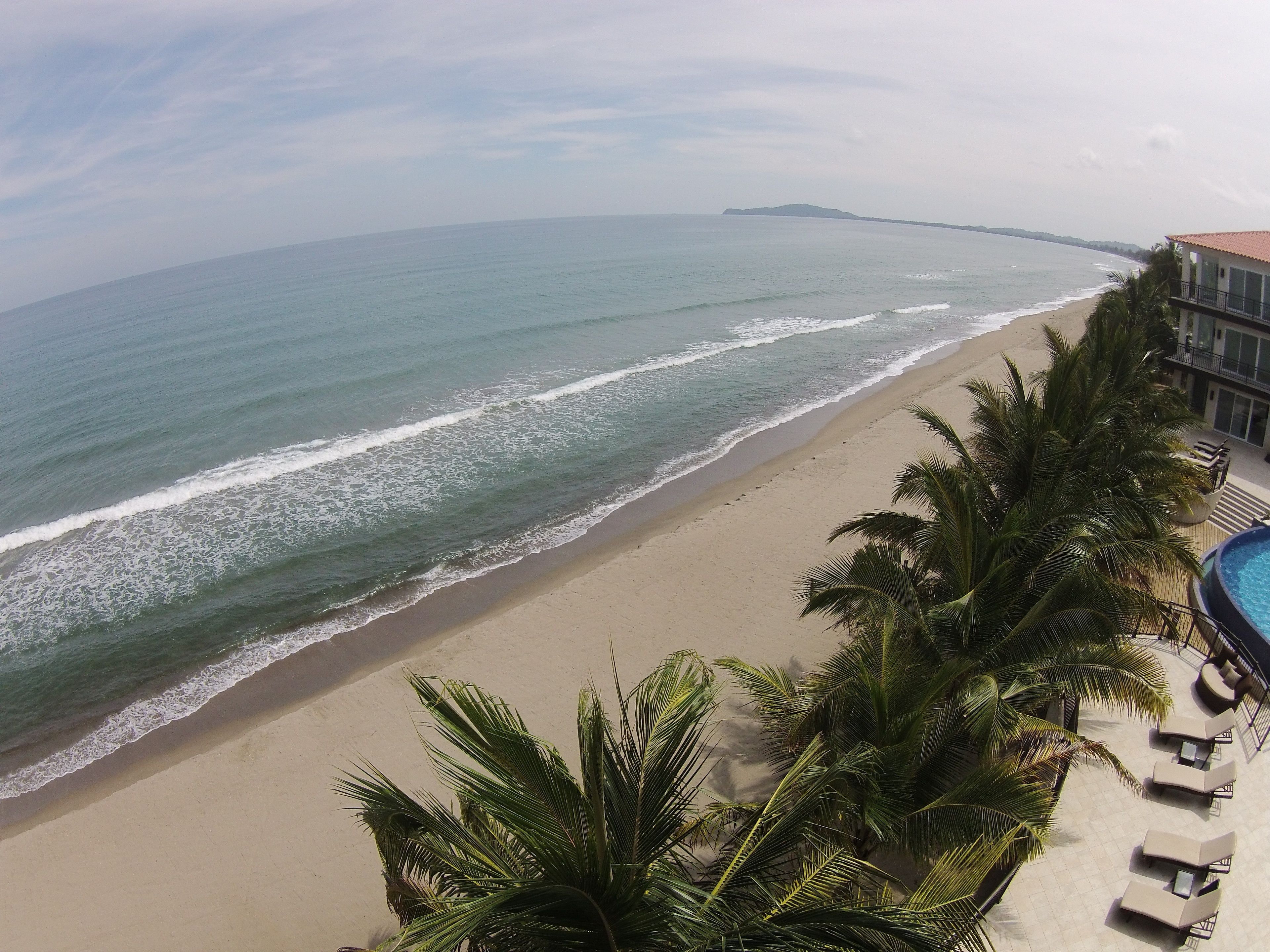 Vista de una playa con zona de piscina, palmeras y una isla distante.