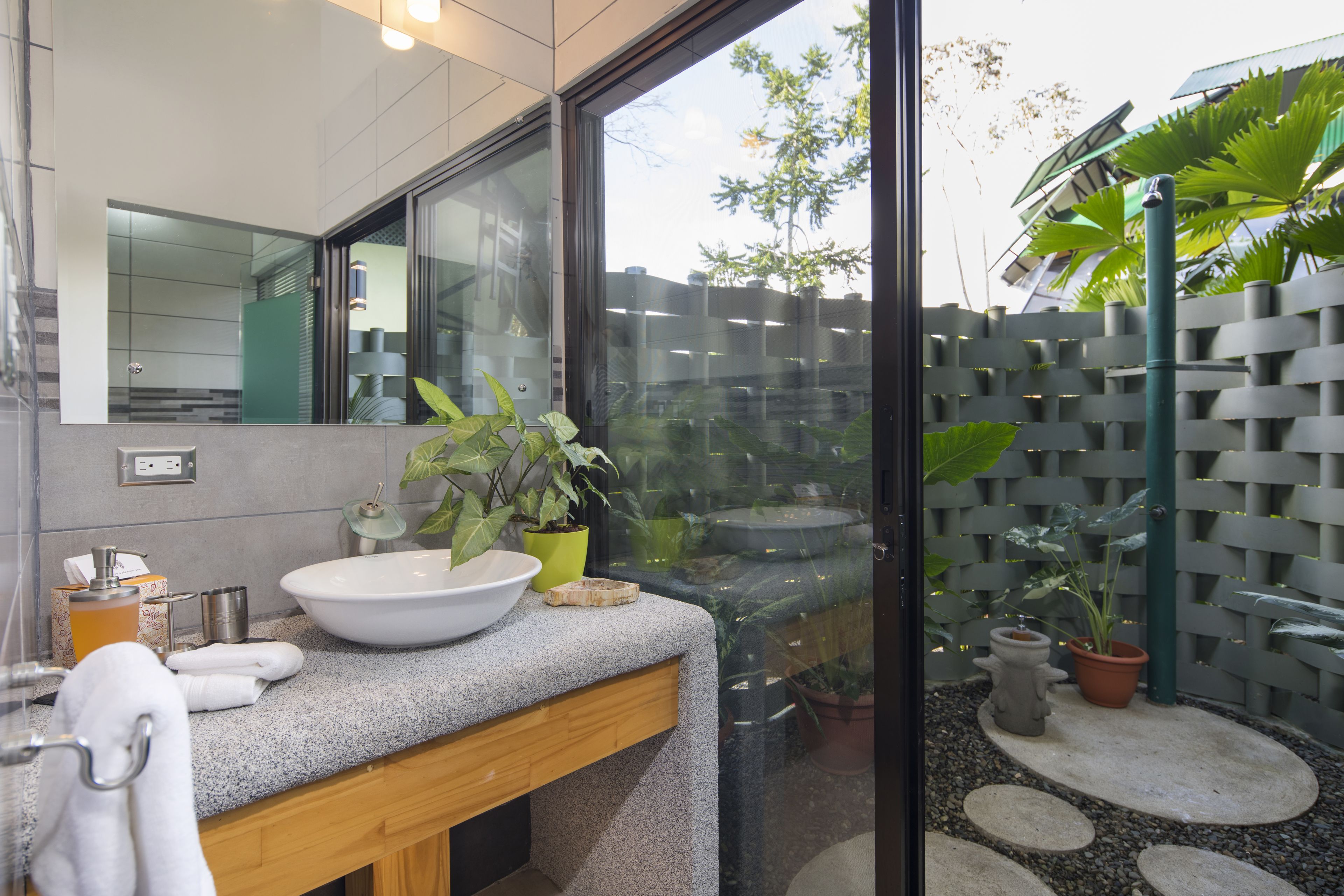 Un baño moderno con un lavamanos grande, un espejo y plantas en macetas.