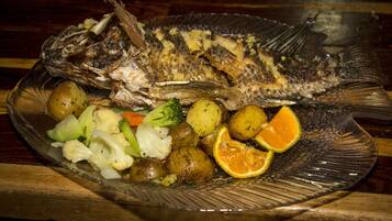 Un pescado entero en un plato con patatas, coliflor y una rodaja de naranja.