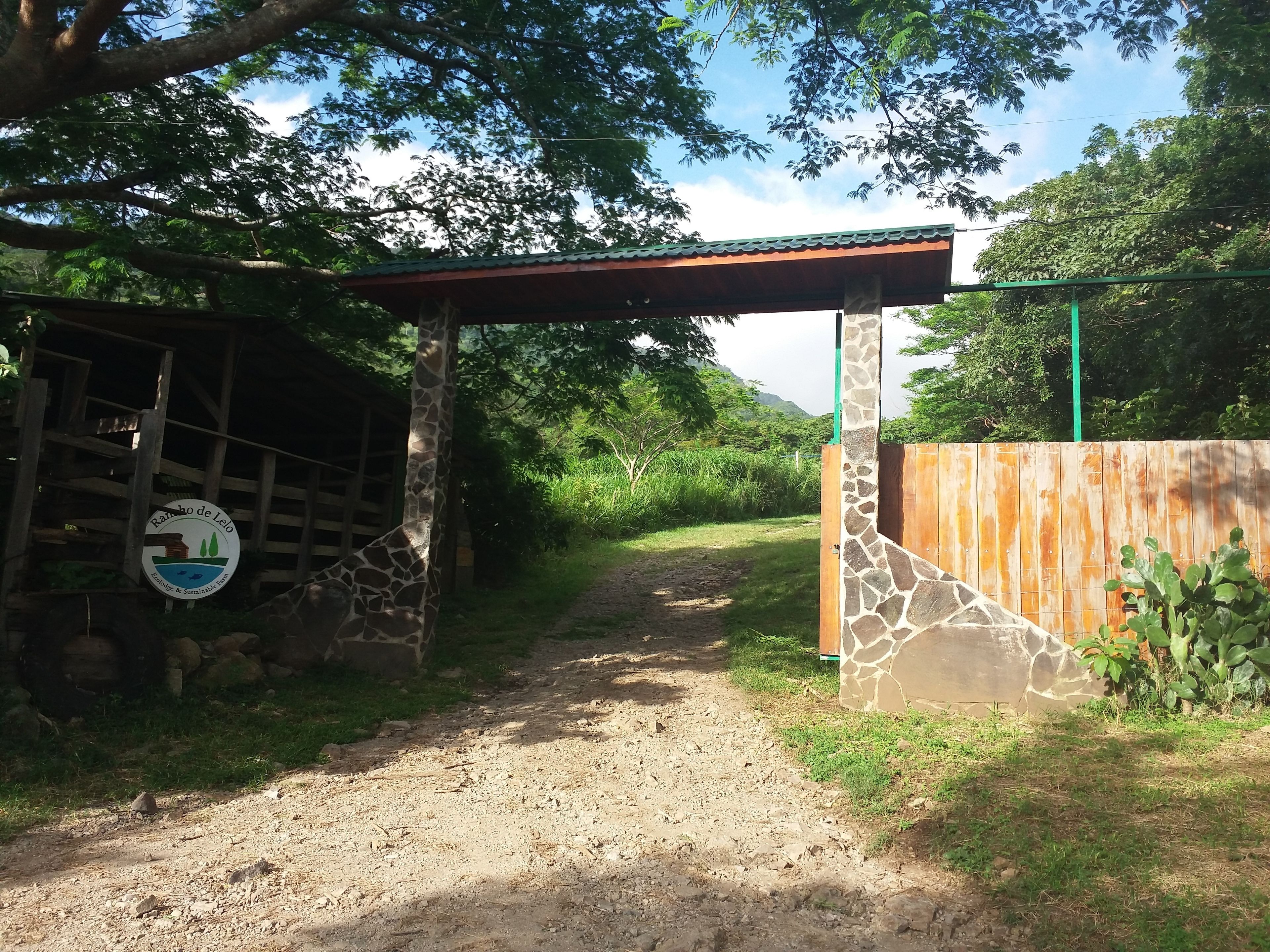 A dirt path leading to a building with a green roof and a stone wall.