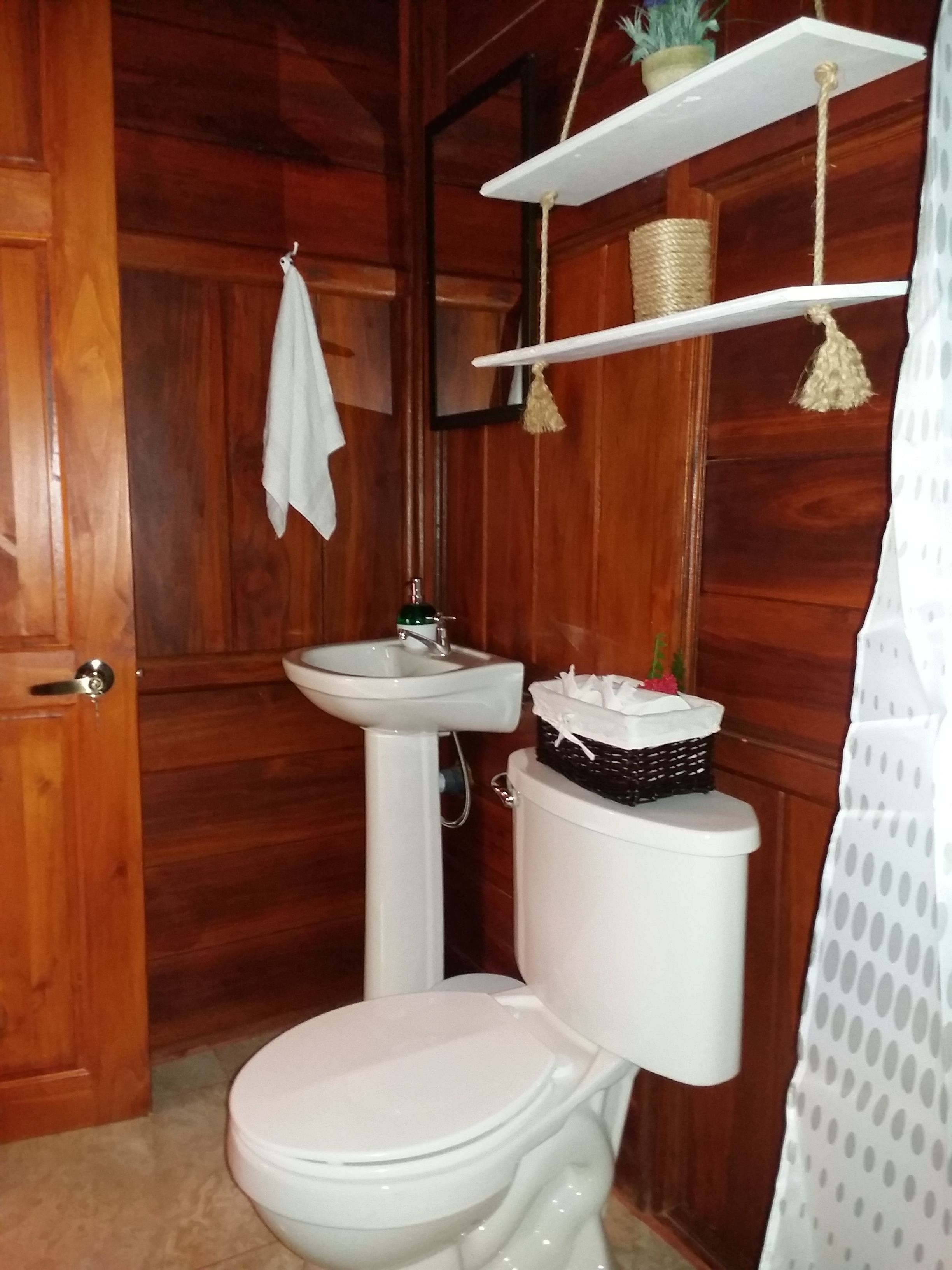 A wooden bathroom with a white toilet, a sink, and a shelf with a basket and a plant.