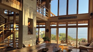 A spacious room with a large wooden table, a staircase, and large windows offering a view of the sea. - La Playa (Los Organos)