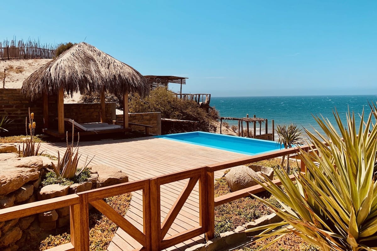 A wooden deck with a pool, a thatched-roof structure, and a view of the ocean.