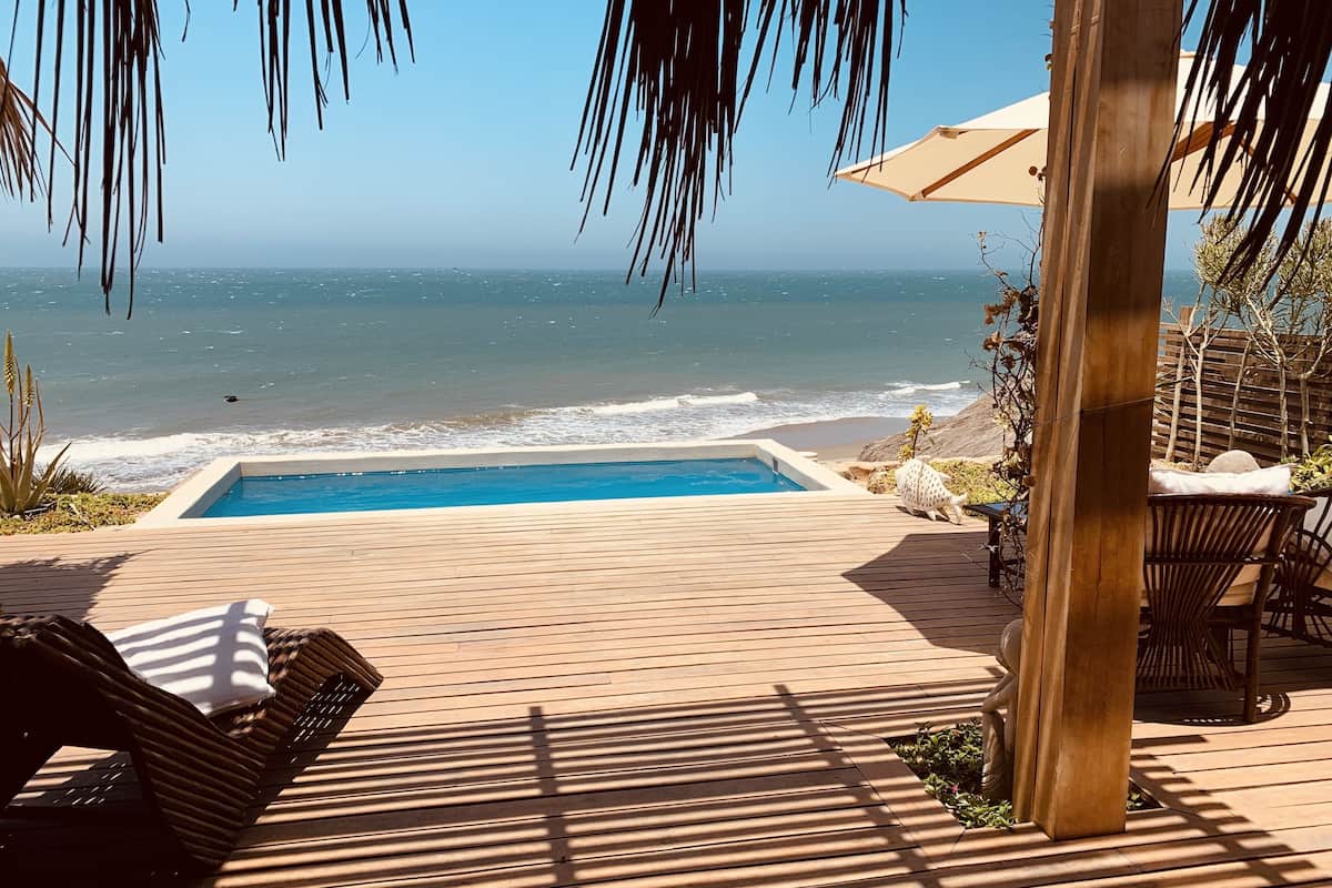 A wooden deck with a swimming pool, lounge chairs, and a view of the ocean.