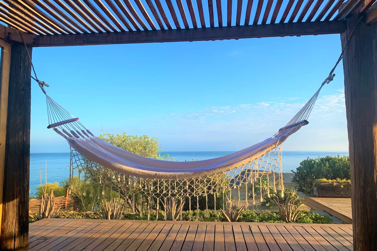 A hammock under a wooden pergola with a view of the sea.