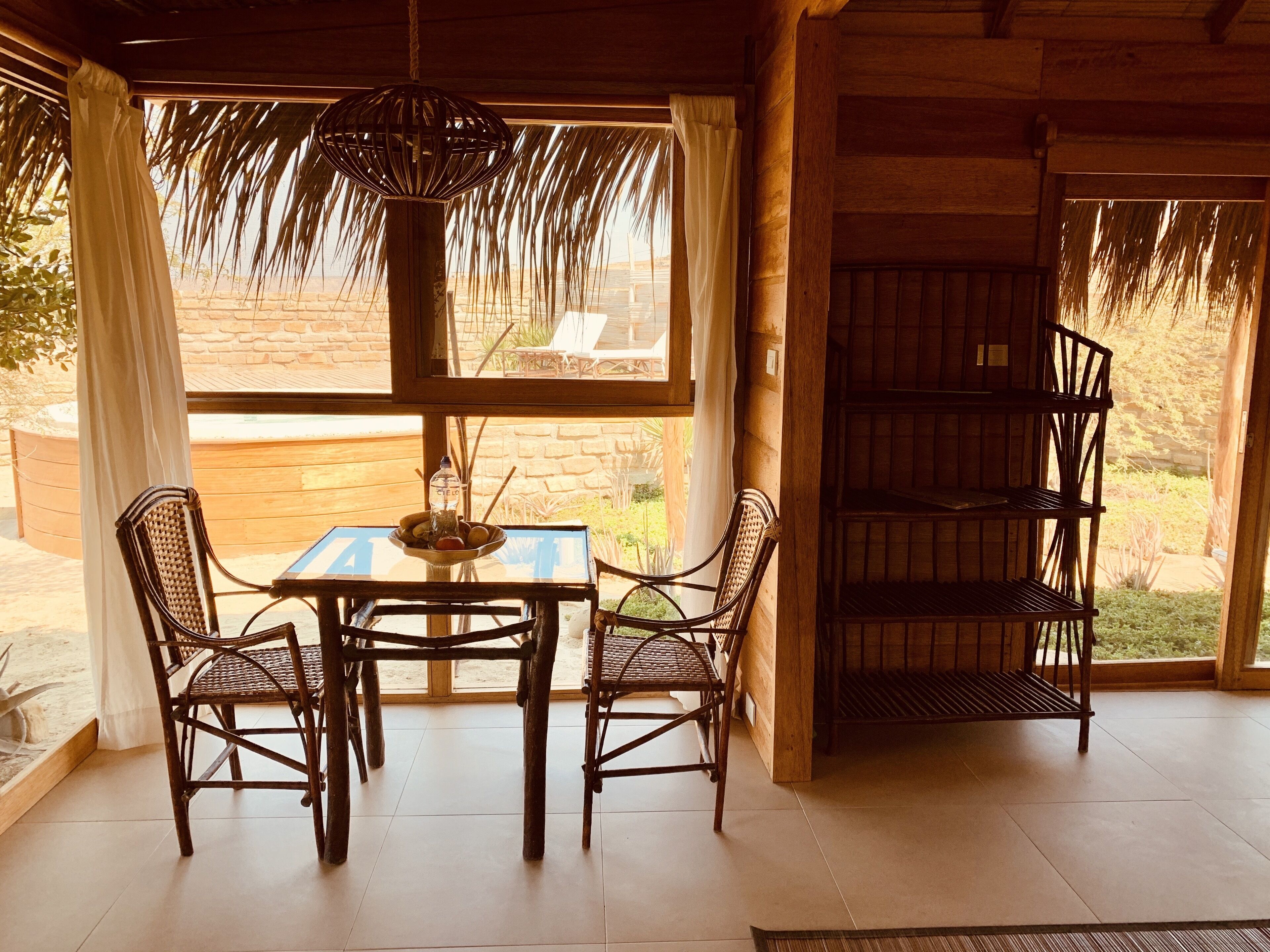 A wooden interior with a glass table and chairs, a hanging light fixture, and a view of the outdoors.