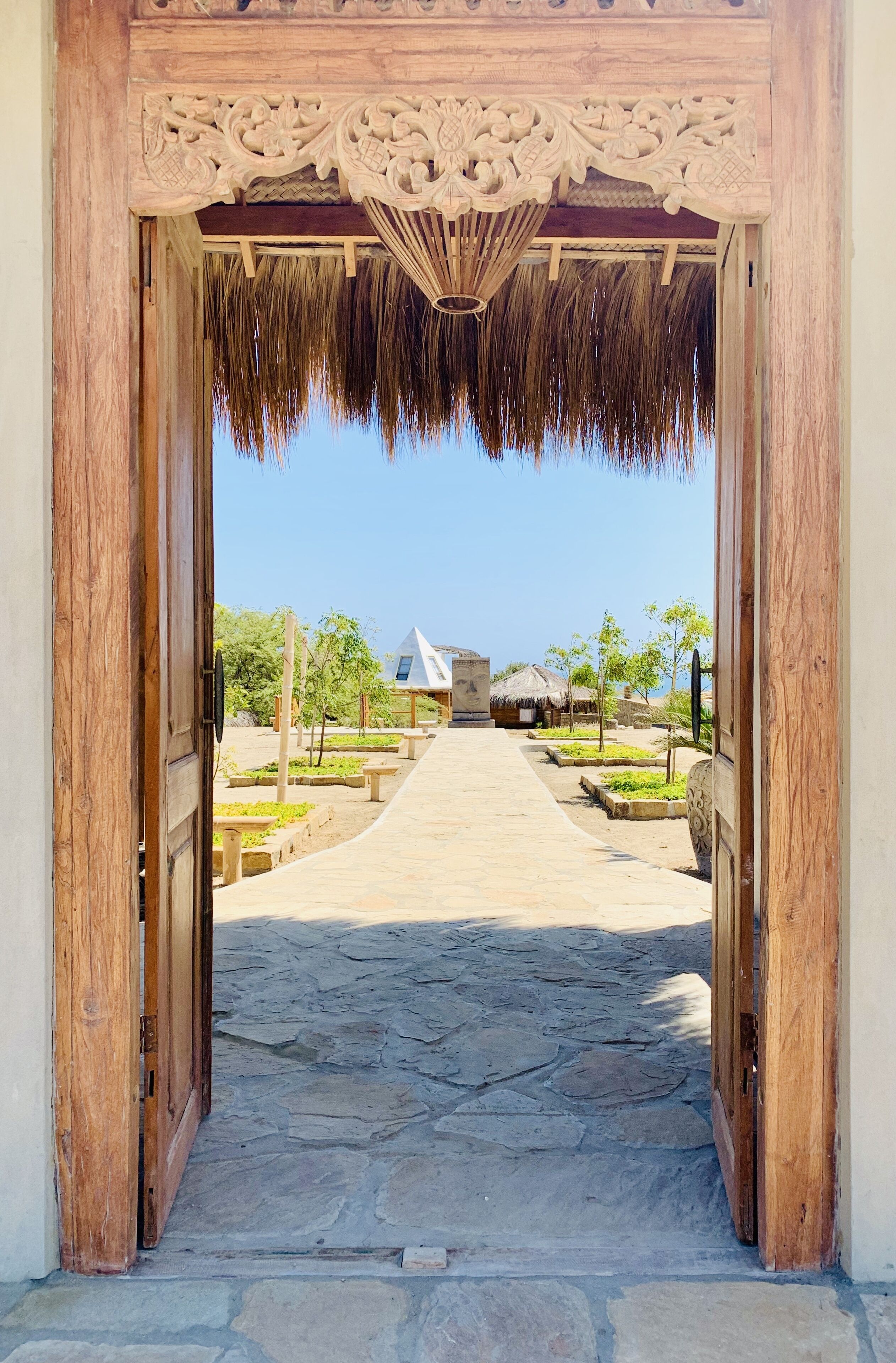 A wooden entrance with a thatched roof leading to a paved pathway.