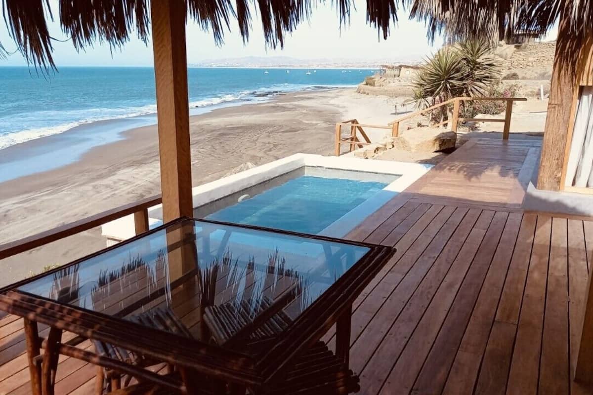 A wooden deck with a glass table and chairs, overlooking a beach and ocean.