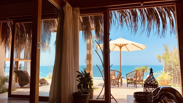 A beachside room with large windows, a potted plant, wicker chairs, and a wooden table. - La Playa (Los Organos)
