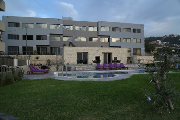 A modern building with a swimming pool, outdoor seating, and a stone facade. - VU'Z Hotel Apt (Blat)