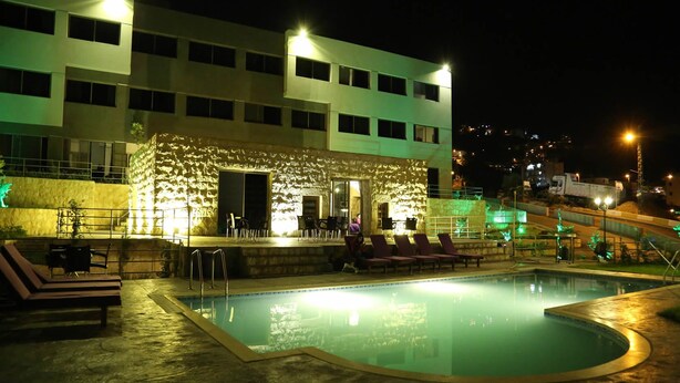A nighttime swimming pool area with lounge chairs, a stone structure with seating, and a building in the background. - VU'Z Hotel Apt (Blat)