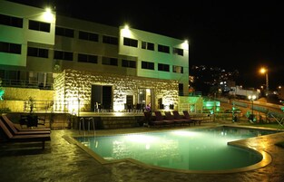 Un área de piscina nocturna con sillones de descanso, una estructura de piedra con asientos y un edificio al fondo.
