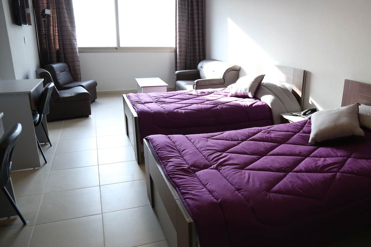 A hotel room with two beds, a desk, a chair, and a small table.