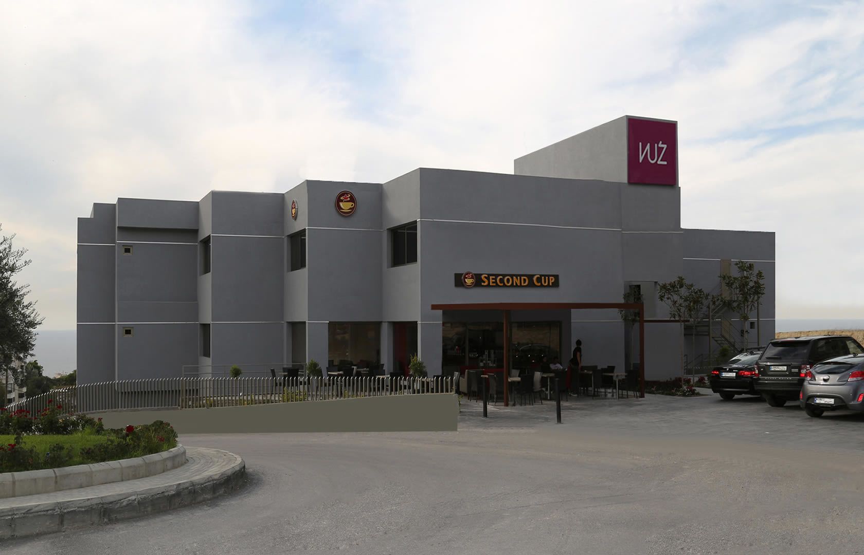Un edificio moderno con un letrero de 'Second Cup', un logo de 'Wuz' y un área de estacionamiento con automóviles.