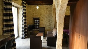 A rustic stone-walled room with a wooden ceiling, a sofa, a coffee table, a television, and a striped curtain. - VU'Z Hotel Apt (Blat)