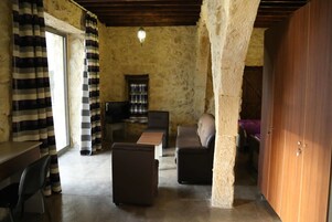 Una habitación rústica con paredes de piedra, techo de madera, un sofá, una mesa de centro, un televisor y una cortina a rayas.