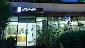 Adana Garden Hotel bygningen med facade, oplyst skiltning, store vinduer og flag.