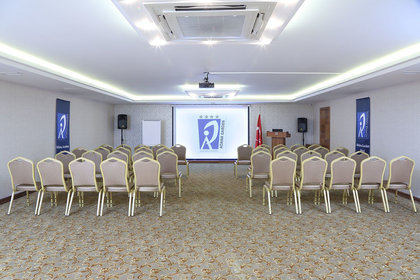 A conference room with rows of chairs, a podium, and a presentation screen.