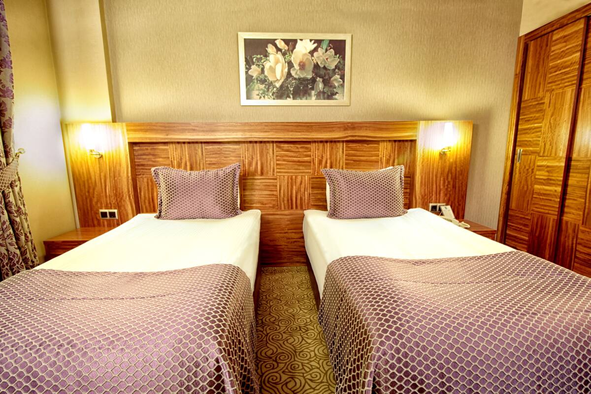 Een hotelkamer met twee enkele bedden, een houten hoofdbord, beddengoed met een patroon, een lijst met bloemkunst boven de bedden en een houten garderobe.