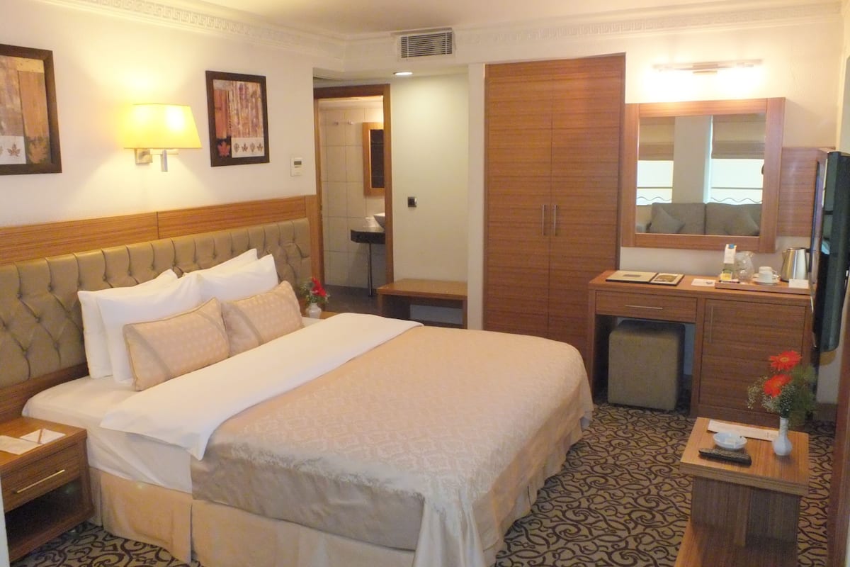 Ein Hotelzimmer mit einem großen Bett, einem Holzschrank, einem kleinen Schreibtisch mit Spiegel und einem Nachttisch.