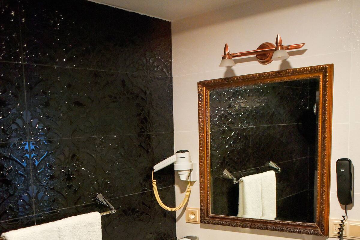 A bathroom with a white sink, black countertop, and a large mirror with a gold frame.